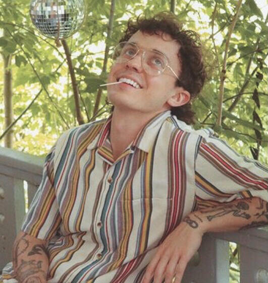 kurtis conner sitting on a bench in front of some leaves he is smiling and looking up